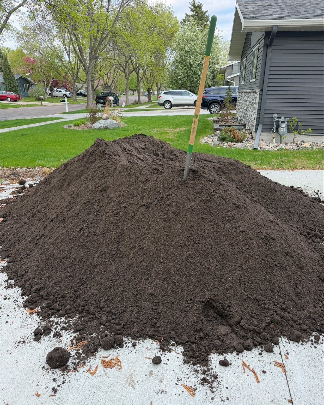 5 cubic yards of Baker premium planting soil sitting in a driveway with a shovel in the middle. 